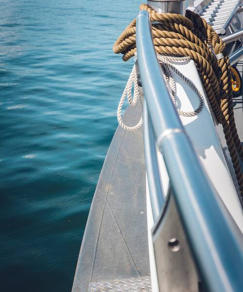 Coiled mooring lines on deck beside a stainless steel railing on board a boat.