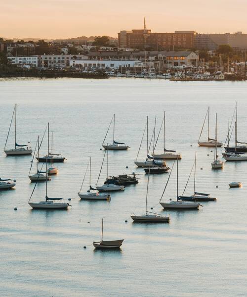 Sailboats anchored on calm water near a harbour at sunset